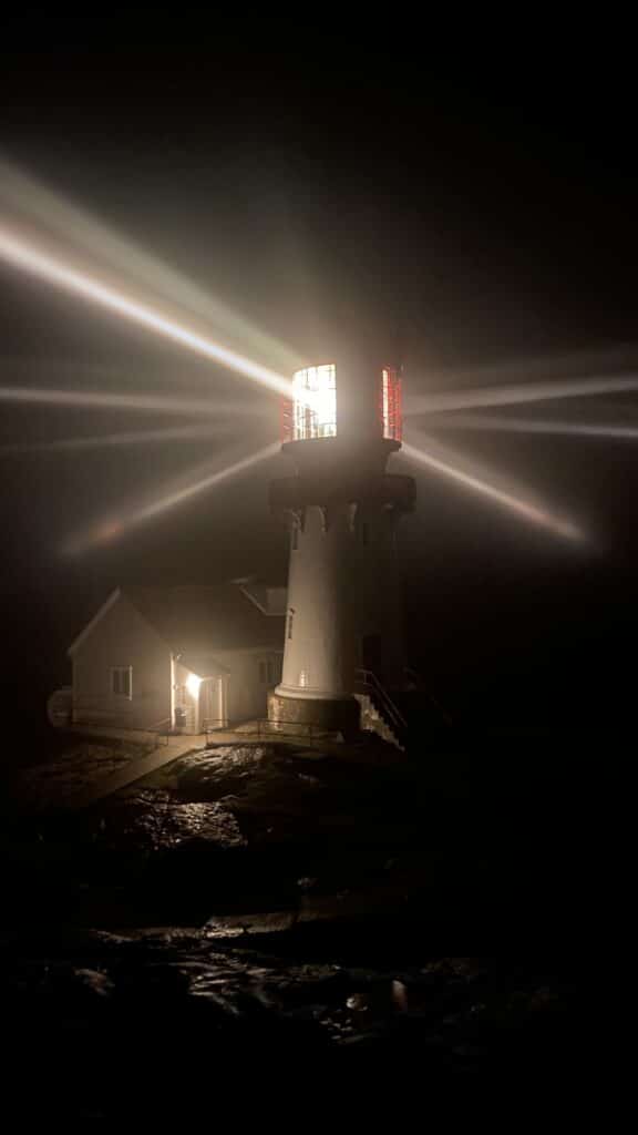Lindesnes fyr i mørket med tent linse og lysstråler som kommer ut fra toppen