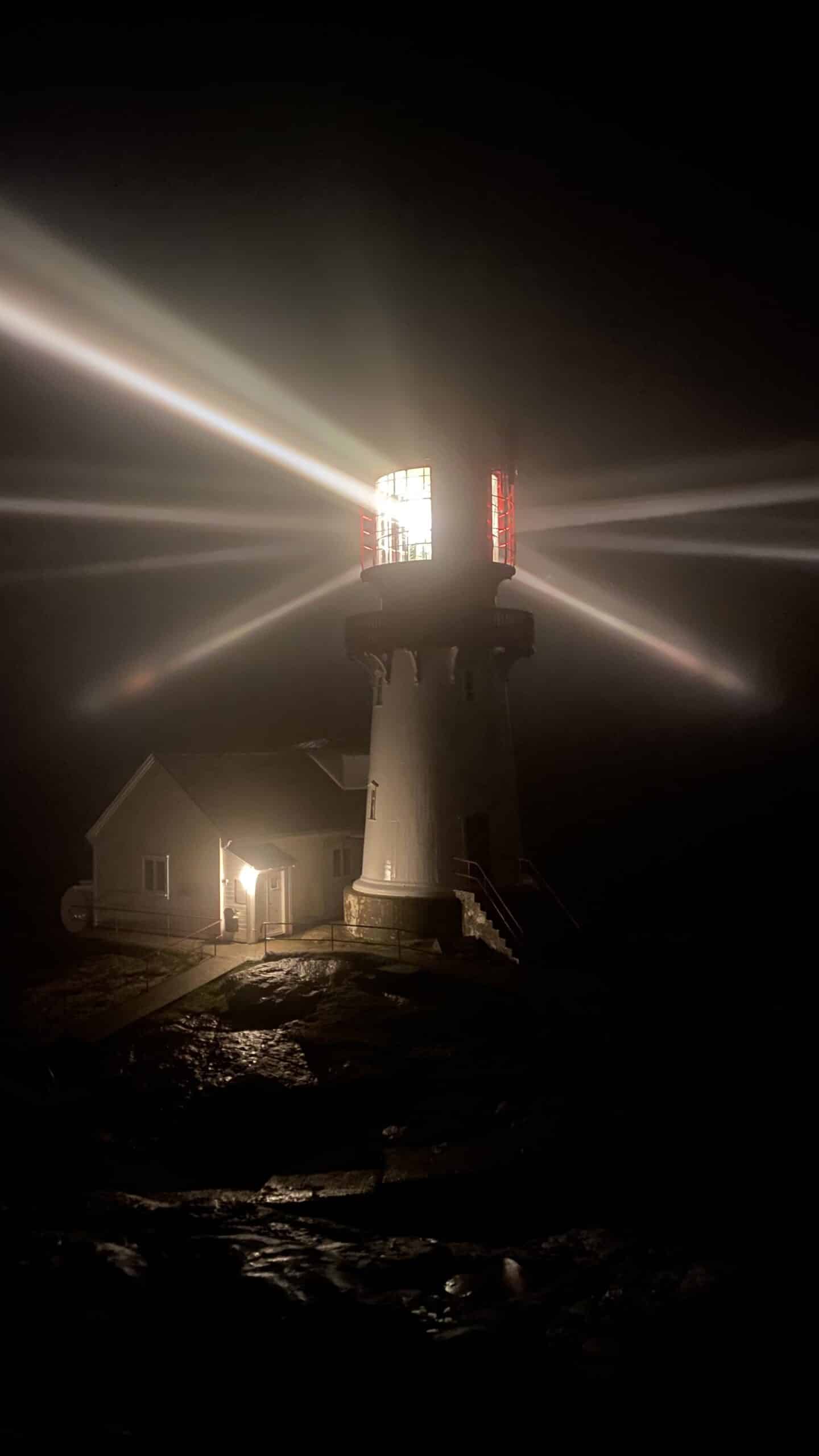 Lindesnes fyr i mørket med tent linse og lysstråler som kommer ut fra toppen
